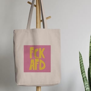 Könnte beinhalten: Eine beige Tragetasche mit einem rosa Quadrat und dem Text "FCK AFD" in gelben Buchstaben.