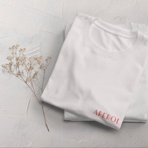 May include: White t-shirt with the word "APEROL" printed in pink on the front.