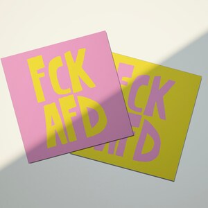 May include: Two square cards with the text "FCK AFD" printed in yellow letters on a pink and yellow background.