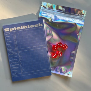May include: A blue scorecard with the word "Spielblock" printed on it. The scorecard is for a dice game and includes categories such as "Ones", "Twos", "Threes", "Fours", "Fives", "Sixes", "3 of a Kind", "4 of a Kind", "Small Street", "Large Street", "Full House", "Chance", and "Yatzy". There are six red dice in a clear plastic bag.