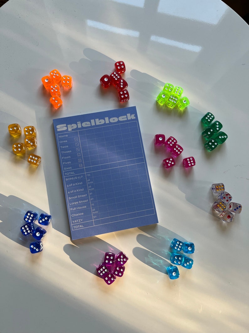 May include: A blue and white scorecard with the word "Spielblock" printed on it.  The scorecard is surrounded by colourful dice with white dots. The dice are red, orange, yellow, green, blue, purple, and gold.