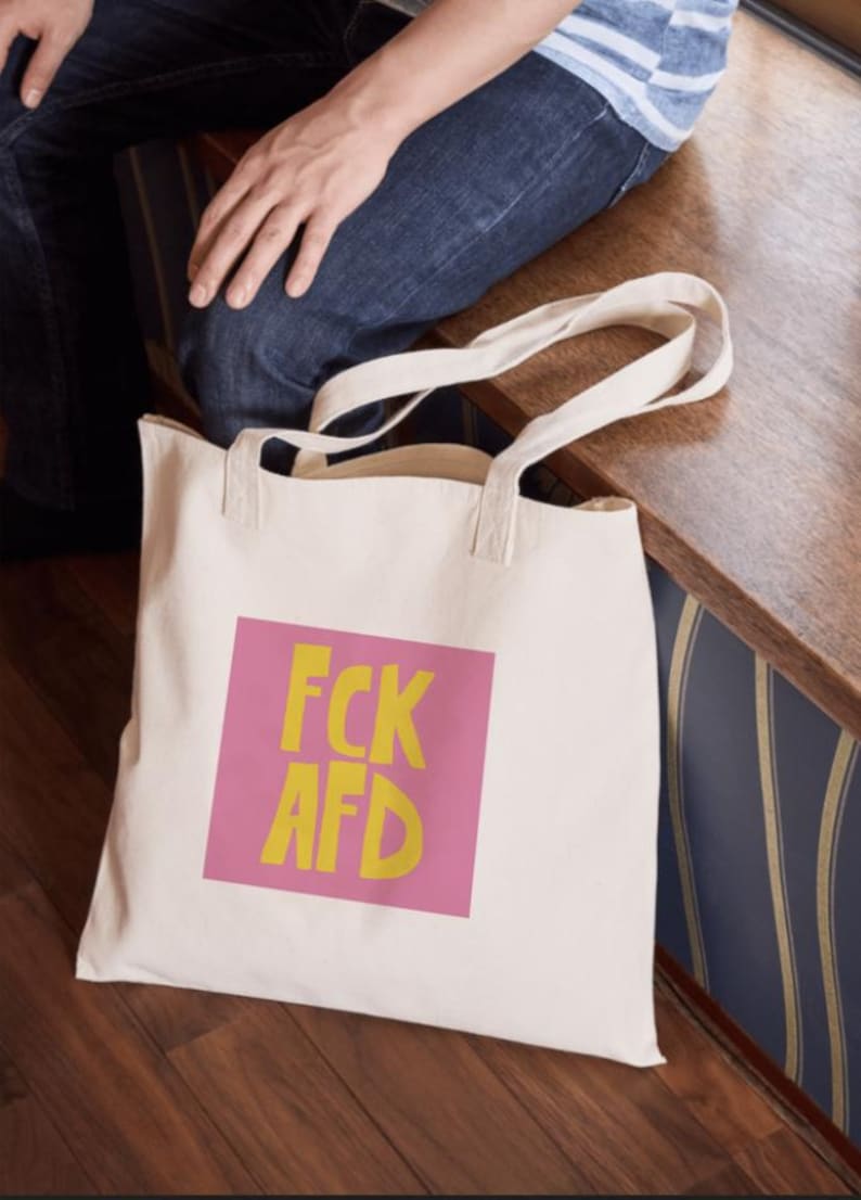 Puede incluir: Una bolsa de lona blanca con texto rosa y amarillo que dice "FCK AFD".