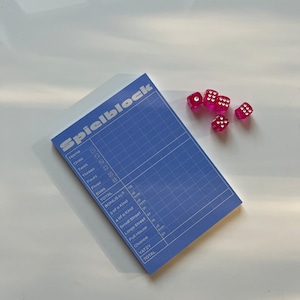 May include: A blue scorecard with the word "Spielblock" printed on it. The scorecard is for a game of Yahtzee and has spaces for recording scores for ones, twos, threes, fours, fives, sixes, three of a kind, four of a kind, small straight, large straight, full house, chance, and Yahtzee. There are five pink dice on the table next to the scorecard.