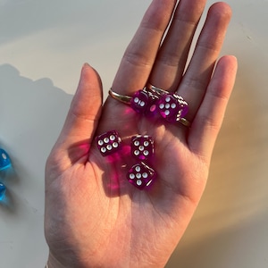 May include: Five purple dice with white dots on each side. The dice are in a person's hand.