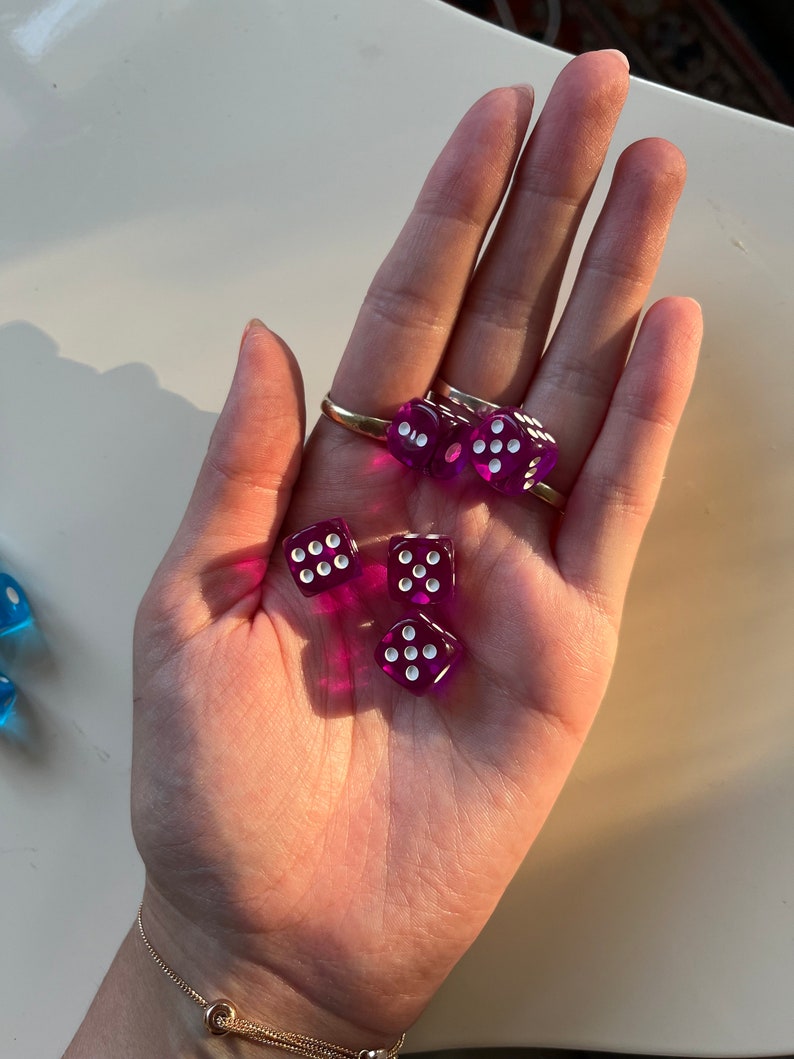 May include: Five purple dice with white dots on each side. The dice are in a person's hand.