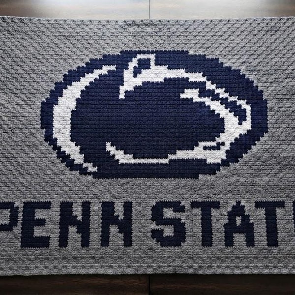 May include: A rectangular crochet blanket featuring a gray background with a dark blue and white Nittany Lion logo centered at the top. The text "PENN STATE" is crocheted in dark blue block letters across the bottom portion of the gray textured fabric.