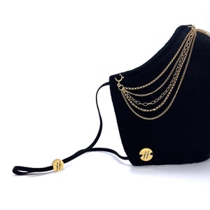 Pu&ograve; includere: Maschera facciale nera con decorazioni a catena dorata e un cinturino elastico nero. La maschera ha un logo circolare dorato con la lettera "H" su ciascuna estremit&agrave; del cinturino.