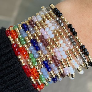 May include: A stack of colorful beaded bracelets with gold spacers. The bracelets are made with various colors of glass beads, including red, orange, green, blue, purple, and white.