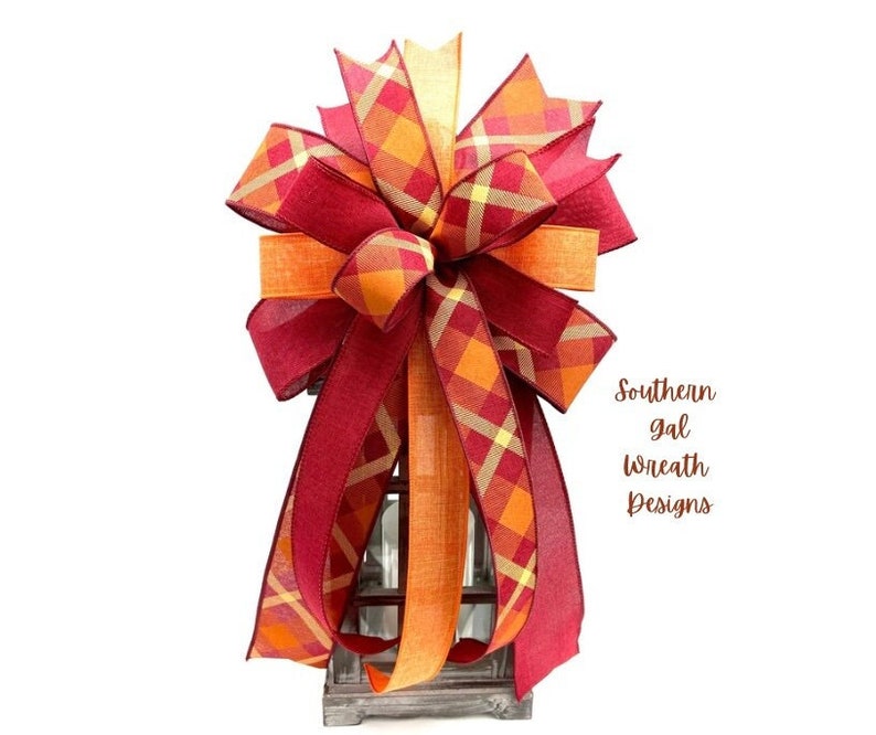 May include: A large, red and orange plaid bow with a gold and white plaid ribbon. The bow is tied around a lantern.