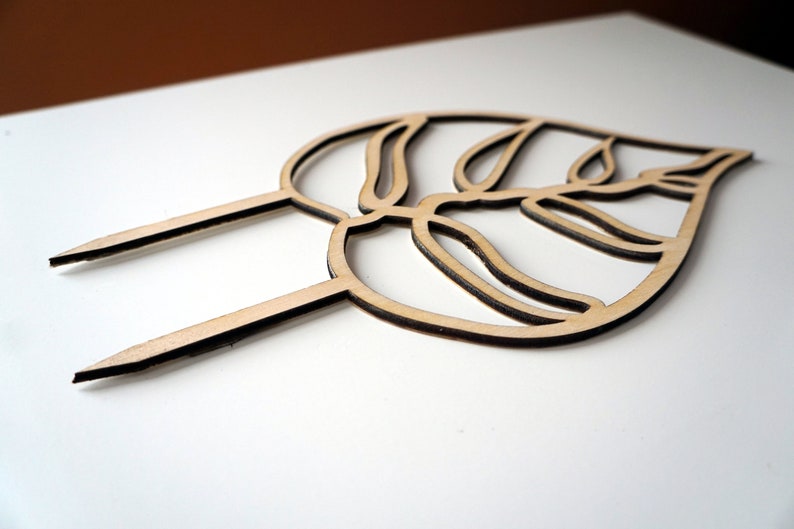 May include: A wooden leaf-shaped cake topper with two pointed stakes. The topper is made of light-colored wood with a dark brown outline, and features a detailed leaf design. Perfect for adding a natural touch to cakes and desserts.