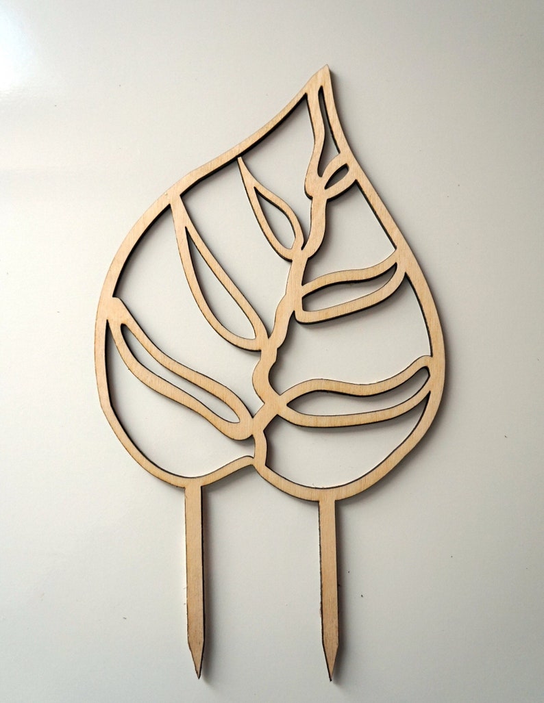 May include: A wooden leaf-shaped garden stake with a cut-out design. The stake features a detailed leaf pattern with two pointed prongs at the base for easy insertion into soil. The natural wood color adds a rustic touch to any garden.