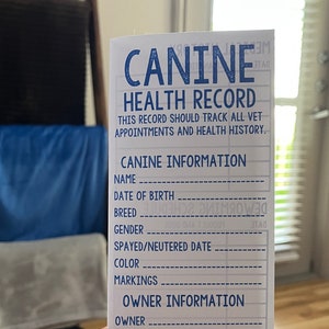 Könnte beinhalten: Eine weiße Karte mit blauem Text, der "Canine Health Record" lautet. Die Karte hat leere Zeilen zum Ausfüllen von Informationen über einen Hund, einschließlich Name, Geburtsdatum, Rasse, Geschlecht, Kastrationsdatum, Farbe, Markierungen, Besitzer, Telefon, Züchter, Züchtertelefon, Erwerbsdatum und Notfallkontakt.