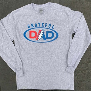 May include: Gray long-sleeve t-shirt with a blue and red oval graphic that says "GRATEFUL DAD" with a lightning bolt design inside the oval.