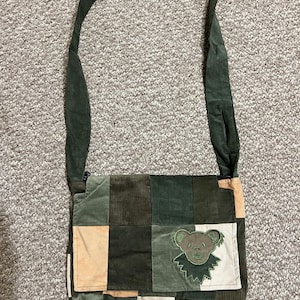 Könnte beinhalten: Eine grüne Patchwork-Schultertasche mit einem braunen Bären-Patch. Die Tasche hat einen langen verstellbaren Riemen.