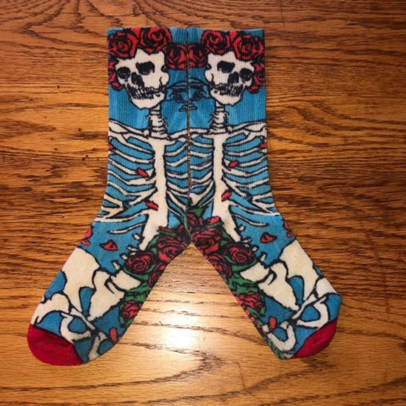 K&ouml;nnte beinhalten: Ein Paar blaue, wei&szlig;e und rote Socken mit einem Skelett- und Rosenmuster. Die Socken zeigen einen Sch&auml;del mit Rosen drumherum.