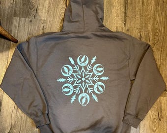 Puede incluir: Una sudadera con capucha marrón con un diseño de copo de nieve azul que presenta un patrón repetido de rayos y una luna creciente.