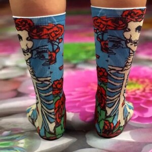 K&ouml;nnte beinhalten: Ein Paar blaue Socken mit einem wei&szlig;en Skelett- und roten Rosen-Motiv.
