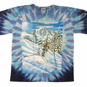 May include: Tie-dye t-shirt featuring a skeleton skiing down a snowy mountain with a Grateful Dead logo in the background.
