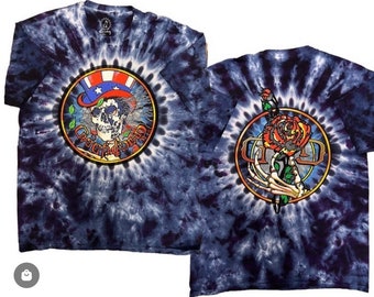 May include: Two tie-dye t-shirts with a Grateful Dead logo. The first shirt features a skull wearing a hat with stars and stripes. The second shirt features a skeleton hand holding a rose.