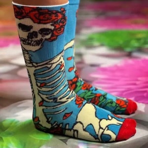 K&ouml;nnte beinhalten: Ein Paar blaue Socken mit einem Totenkopf- und Skelett-Design. Der Totenkopf tr&auml;gt eine Krone aus roten Rosen. Die Socken haben einen roten Saum oben und unten.