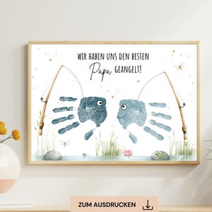 Könnte beinhalten: Gerahmter Druck mit zwei Handabdruck-Fischen mit Angelruten vor einem Aquarellhintergrund. Der Text oben lautet "Wir haben uns den besten Papa geangelt!" und unten "ZUM AUSDRUCKEN".