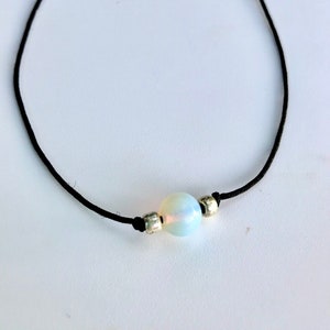 May include: A simple black choker necklace with a single iridescent opal bead and silver accents.