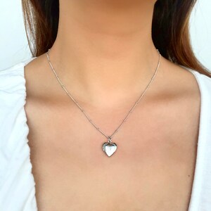 May include: A silver heart-shaped locket necklace on a delicate chain. The locket has a detailed design and is a classic piece of jewelry.