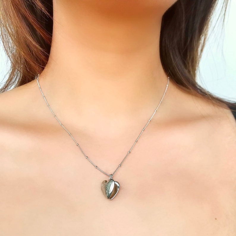 May include: A silver chain necklace with a heart-shaped locket pendant.