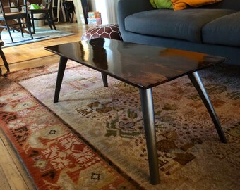 May include: A dark brown wooden coffee table with a glossy finish and black metal legs. The table is sitting on a patterned rug in a living room.