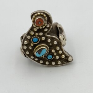 May include: A silver ring featuring a bird design. The ring is adorned with turquoise and red stones.