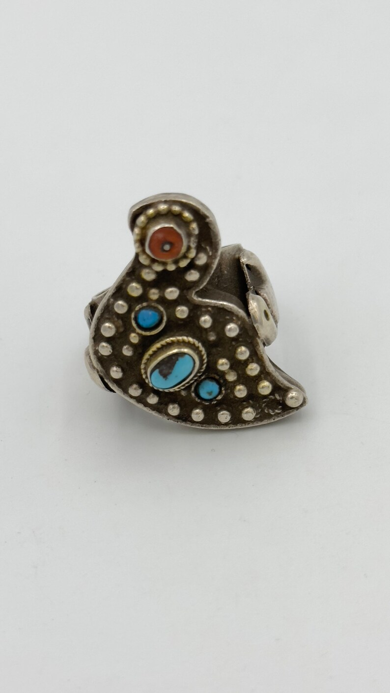 May include: A silver ring featuring a bird design. The ring is adorned with turquoise and red stones.