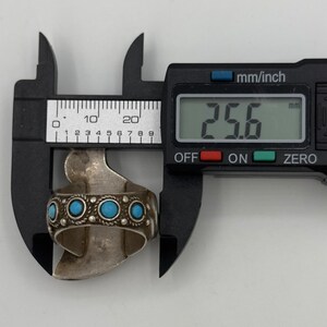 May include: A silver ring with turquoise stones and intricate detailing, measured at 25.6 mm in diameter.