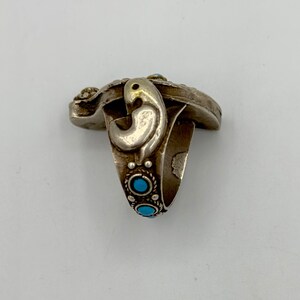 May include: A silver ring featuring a turquoise stone and intricate detailing. The ring has a bird-like design on the side.