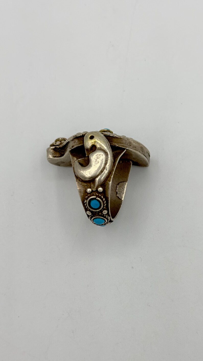 May include: A silver ring featuring a turquoise stone and intricate detailing. The ring has a bird-like design on the side.
