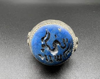 Può includere: Un anello d'argento con una pietra blu incastonata al centro. La pietra presenta un design intagliato di un uccello con dettagli intricati.