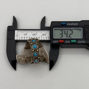 May include: A silver ring with turquoise stones, measured at 34.2 mm in diameter, using a digital caliper.