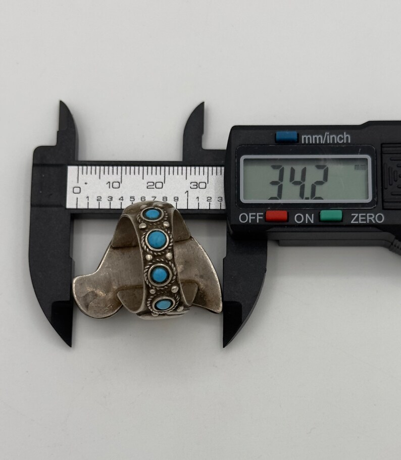 May include: A silver ring with turquoise stones, measured at 34.2 mm in diameter, using a digital caliper.