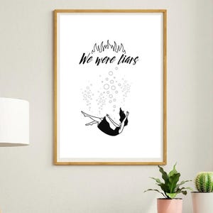 Può includere: Una stampa artistica incorniciata con un'illustrazione in bianco e nero di una persona che cade. Il testo "We were liars" è sopra la figura. Bolle e fiamme sono anch'esse raffigurate. La cornice è di colore marrone chiaro.
