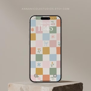 May include: A smartphone displaying a colourful checkered wallpaper with floral and bow designs. The time is 11:45.