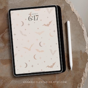 Puede incluir: Un iPad blanco con un fondo beige con un patrón de murciélagos, estrellas y medias lunas. La hora se muestra como 6:17. El texto "ANNANICOLESTUDIOS.ETSY.COM" está en la parte inferior de la pantalla.