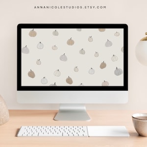 May include: A computer desktop with a light beige background and a pattern of light brown, gray, and white pumpkins. The computer is on a light wood desk with a white keyboard, a brown stone bookend, a stack of books, and a white coffee mug.