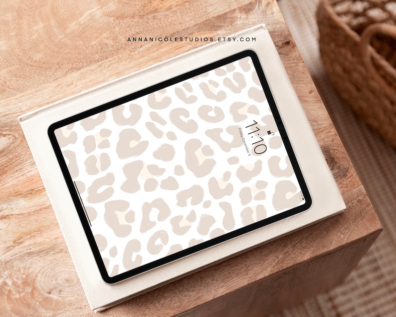 以下が含まれることがあります： ベージュのヒョウ柄の壁紙が貼られた白いiPad。時間は11:10で、日付は12月4日金曜日。iPadは木製のテーブルの上に置かれている。