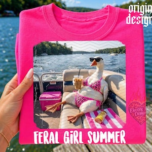 May include: A hot pink t-shirt featuring a graphic of a goose wearing sunglasses and a bikini, holding a drink, and sitting on a boat. The text "FERAL GIRL SUMMER" is at the bottom.