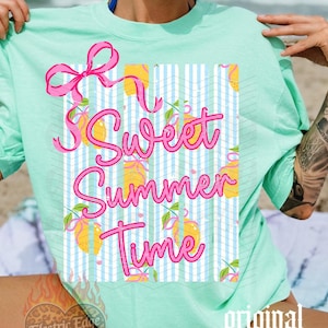 May include: A light green t-shirt with the words "Sweet Summer Time" in pink script. The design includes a pink bow and lemons on a blue and white striped background. The shirt is a relaxed fit.