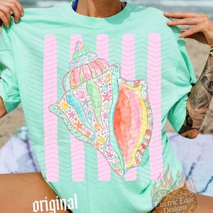 May include: A light green t-shirt featuring a large, colorful seashell design with pink vertical stripes. The seashell is detailed with various sea creatures and vibrant colors. The text "original designer" is visible.