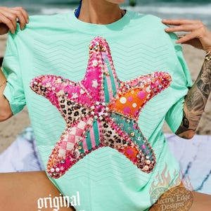 May include: A light green t-shirt featuring a large, colorful starfish design. The starfish is made of various patterned fabrics, including pink, orange, and leopard print. The shirt has the words "original designer" printed on it.