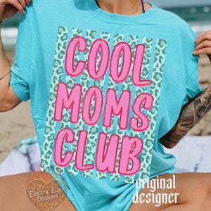 Comfort Colors Mockup. May include: A turquoise t-shirt with the words "COOL MOMS CLUB" in pink, outlined in a darker pink. The text is set against a background of teal stripes and a leopard print pattern. The shirt is a casual style.