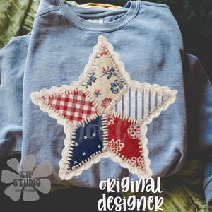 Può includere: Felpa azzurra con un'applicazione a forma di stella. La stella è realizzata con vari tessuti fantasia nei colori rosso, bianco e blu, con un bordo in pizzo. Il testo "original designer" è visibile.