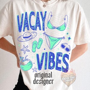 Pode incluir: Camiseta creme com as palavras "VACAY VIBES" em azul, juntamente com ilustra&ccedil;&otilde;es com tema de praia em azul e verde. A camisa tamb&eacute;m apresenta o texto "original designer" em preto.