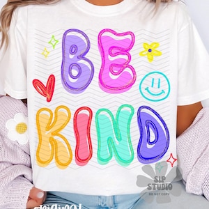 May include: White t-shirt with the words "BE KIND" in colorful bubble letters. The design includes a red heart, a yellow flower, a smiley face, and stars. The shirt is part of a casual wear collection.